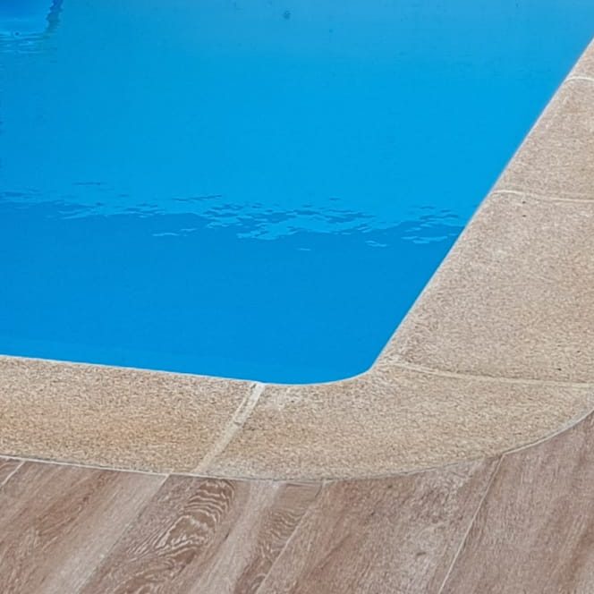  piscina con agua azul y borde de piedra clara sobre un suelo de textura madera.